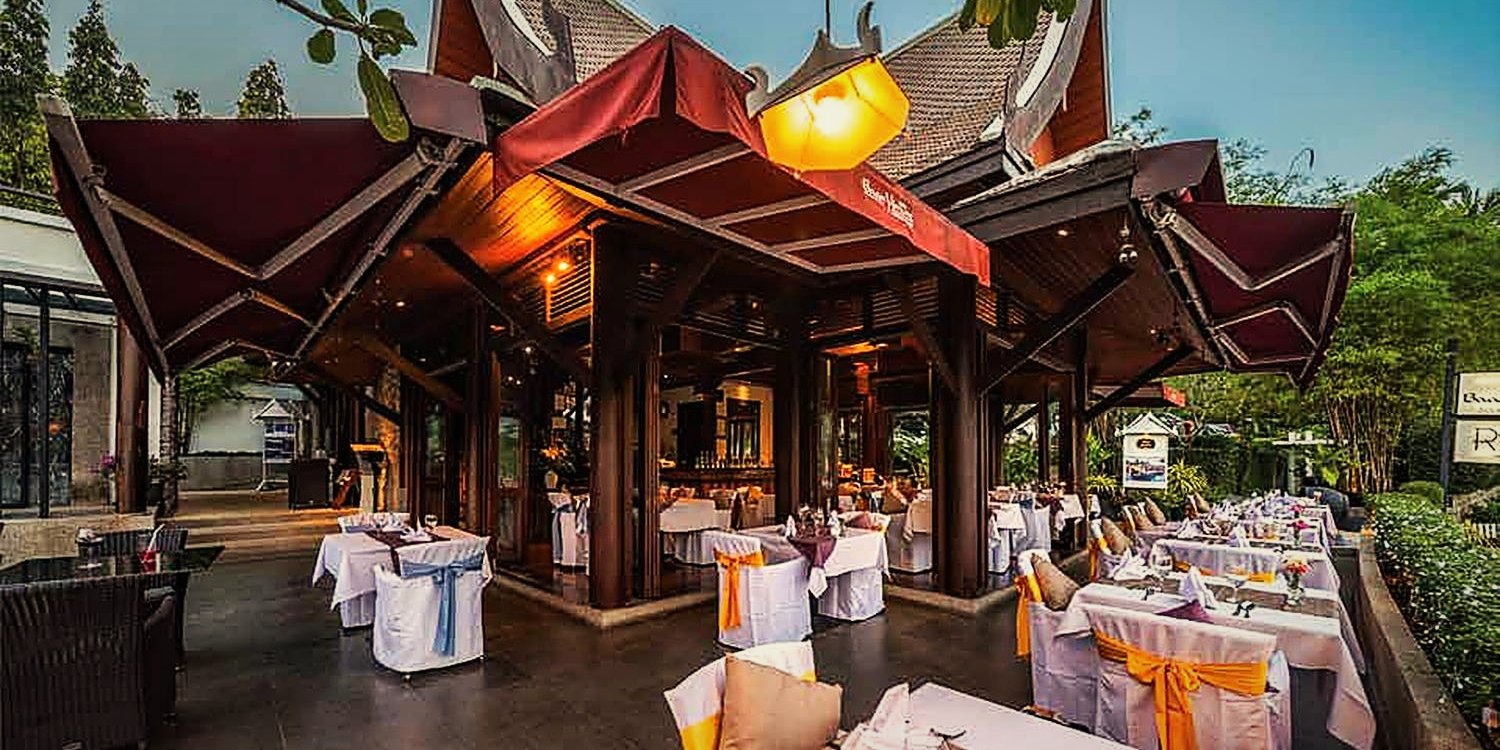 The RICE sala at dusk: teak pavilion with a lit lantern, tables laid in white and saffron on the terrace
